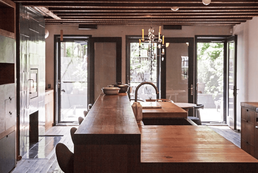 Modern kitchen with wooden countertops, bar stools, and glass doors leading to a garden patio.