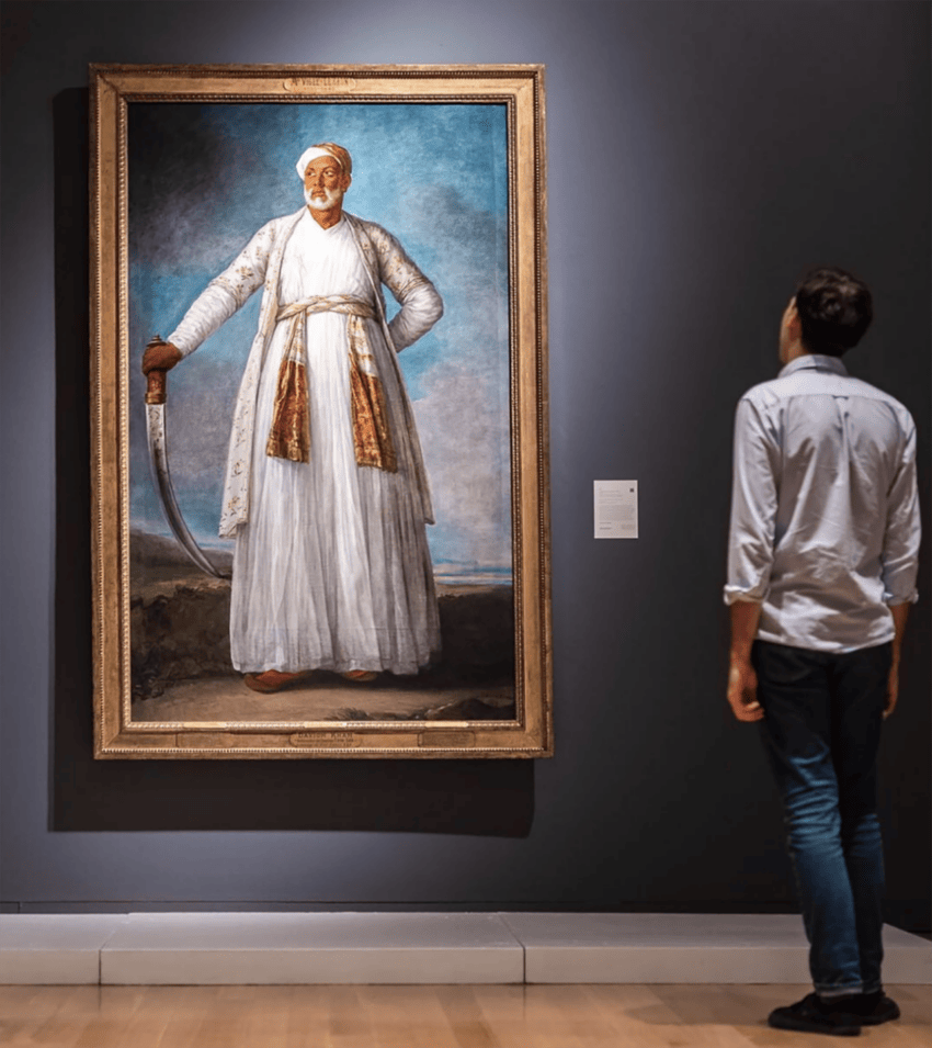 Person observing a large portrait of a historically dressed figure with a sword in a museum gallery setting.