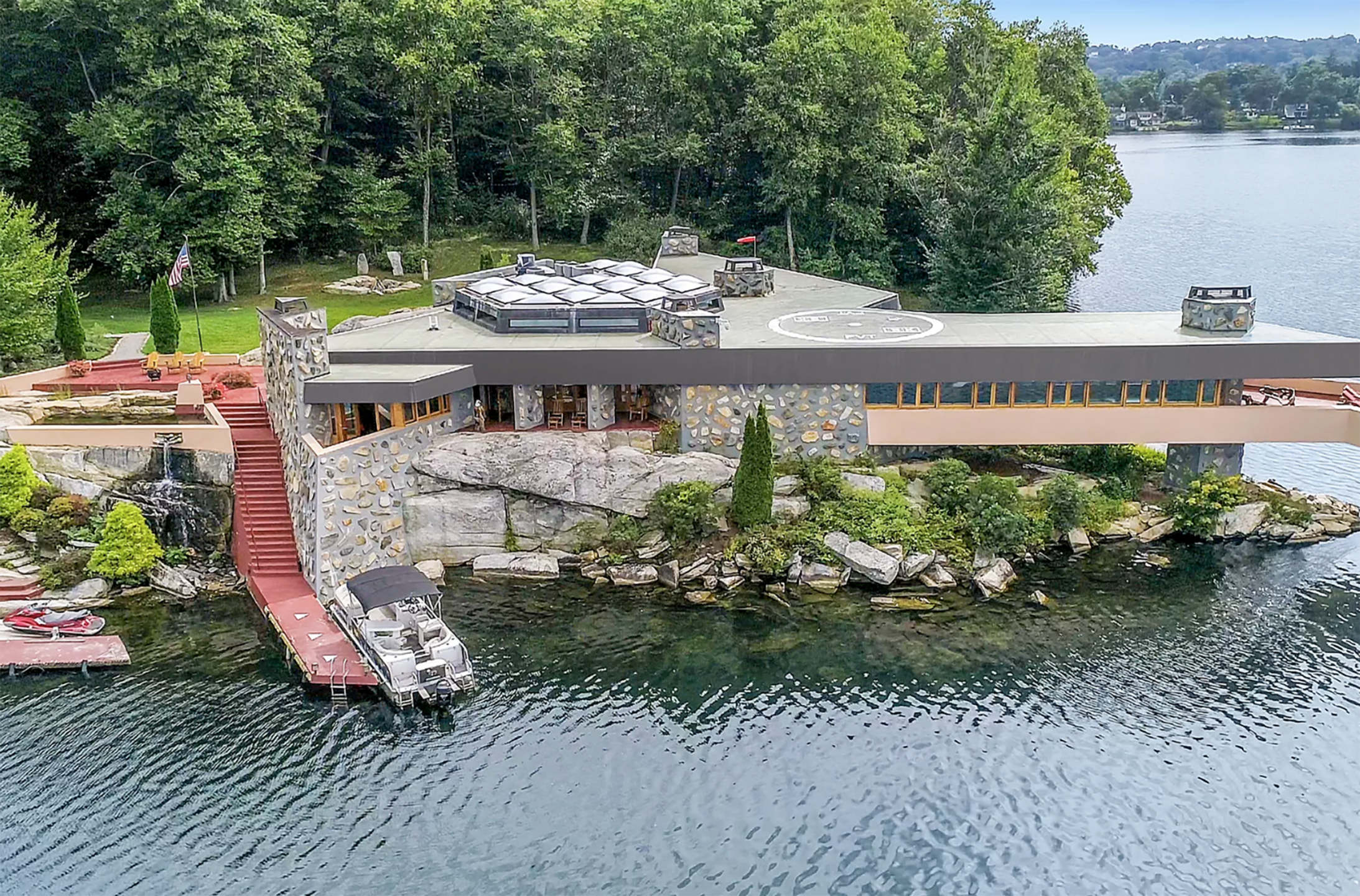 A modern lakeside house with a boat dock, surrounded by trees and water.