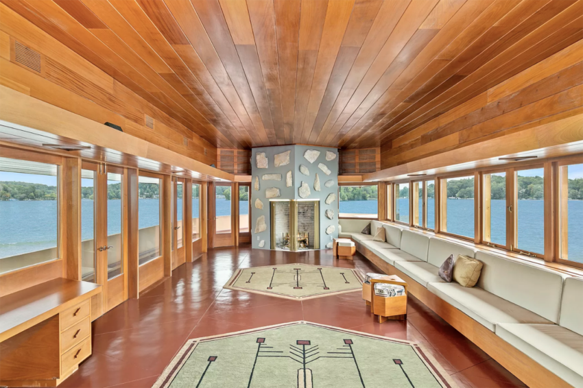 Spacious room with wood paneling, large windows overlooking a lake, modern fireplace, and white seating area.