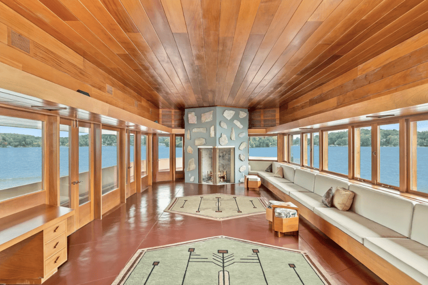 Spacious room with wood paneling, large windows overlooking a lake, modern fireplace, and white seating area.