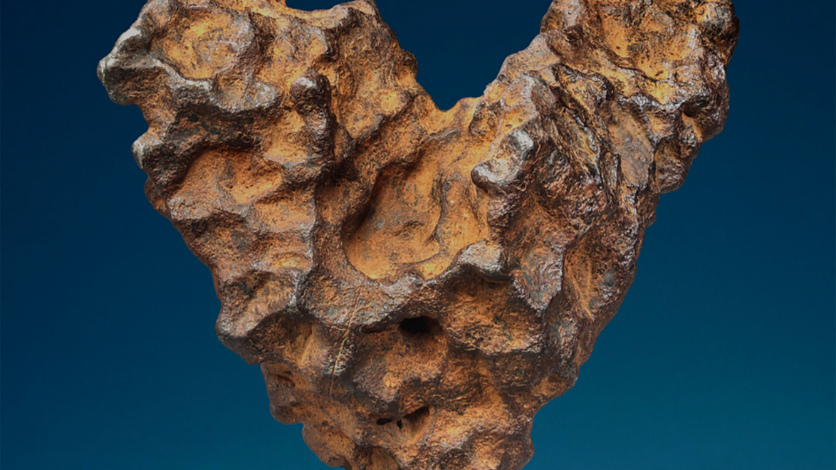 Rust-colored, heart-shaped meteorite with a rough texture against a dark blue background.