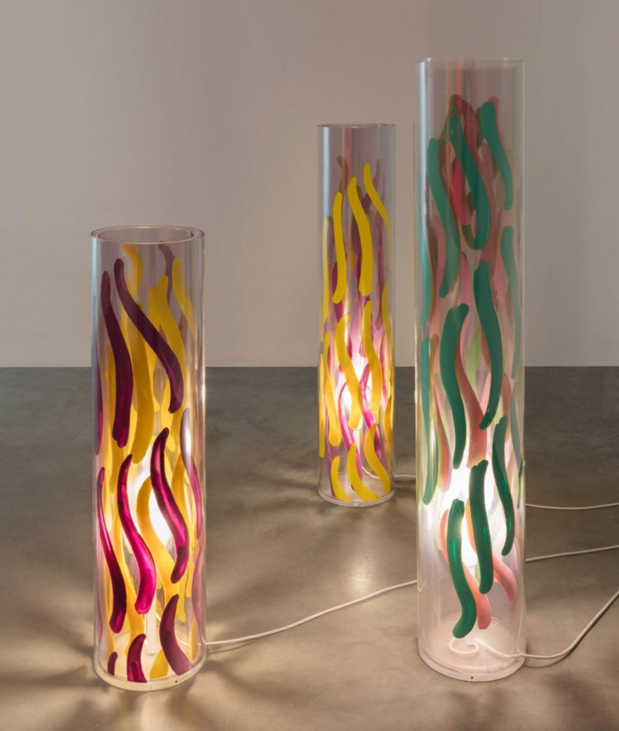 Three cylindrical lamps with colorful abstract designs on a concrete floor.