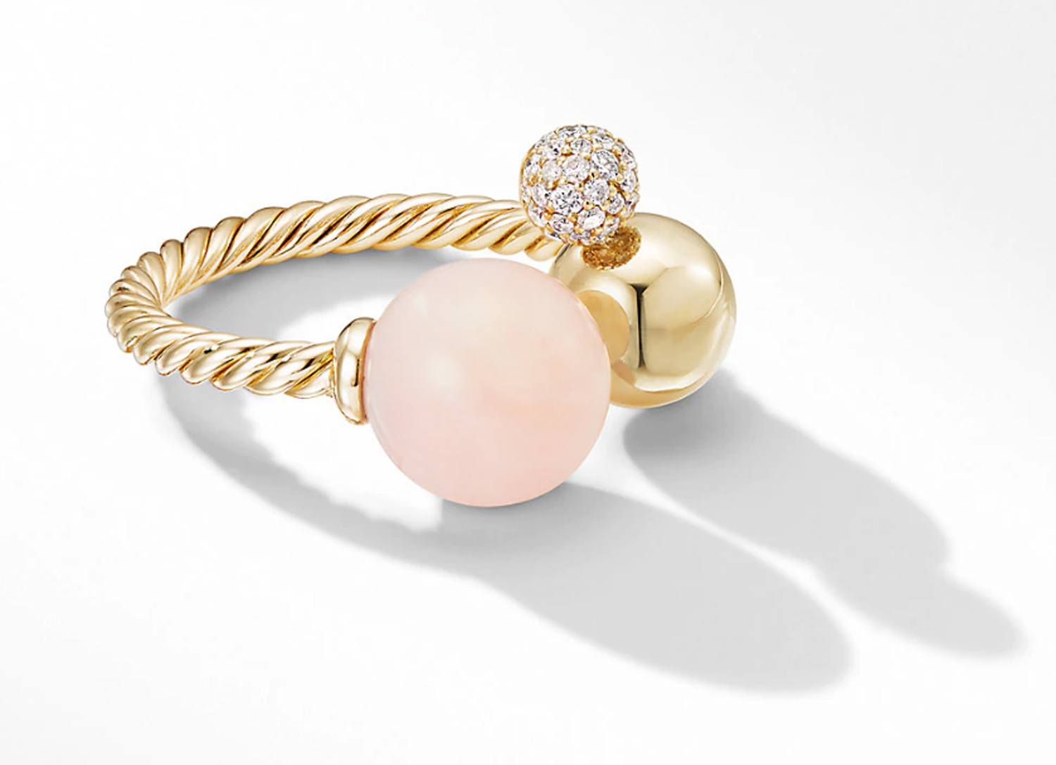 Gold twisted ring with a peach gemstone and a diamond-encrusted sphere on a white background.