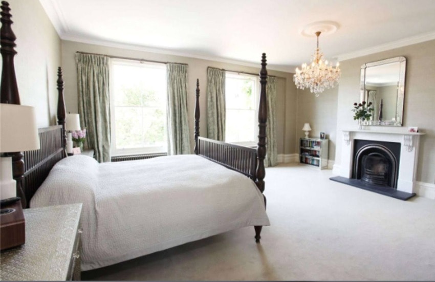 Spacious bedroom with a four-poster bed, chandelier, large windows, and a fireplace with a mirror above it.