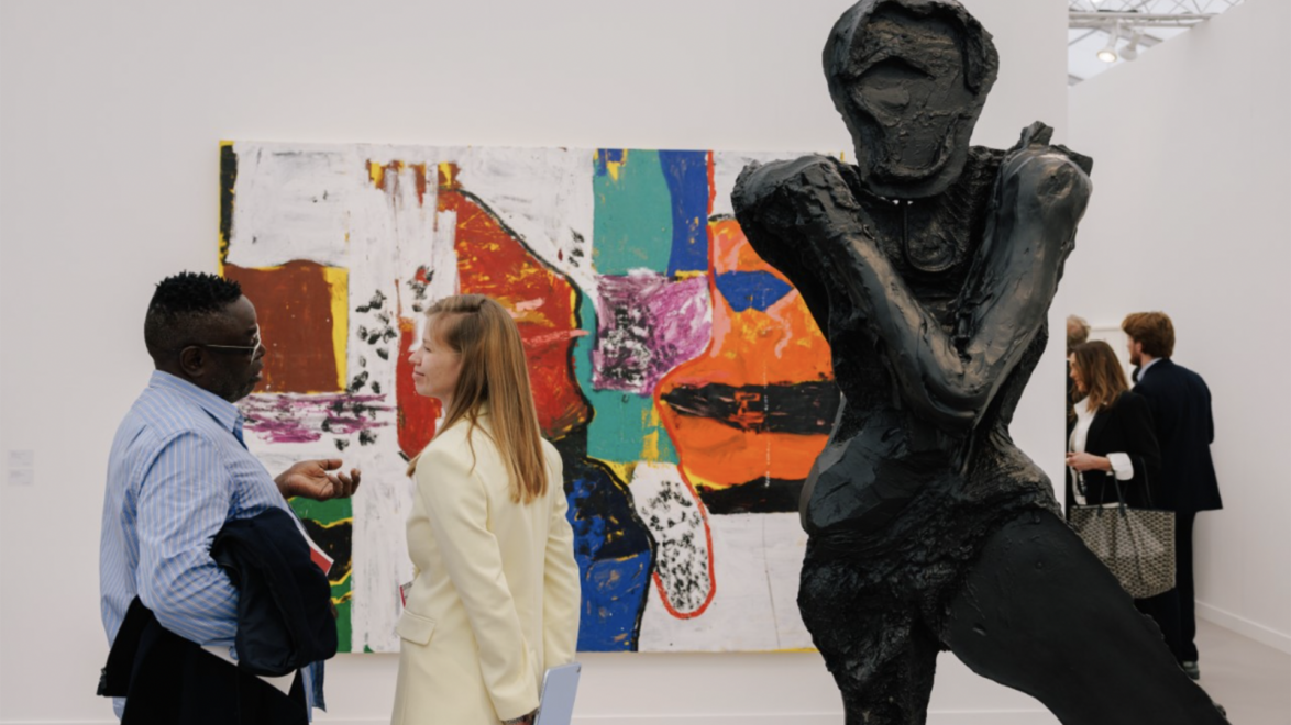 People viewing modern art in a gallery; a large dark sculpture stands prominently in the foreground.