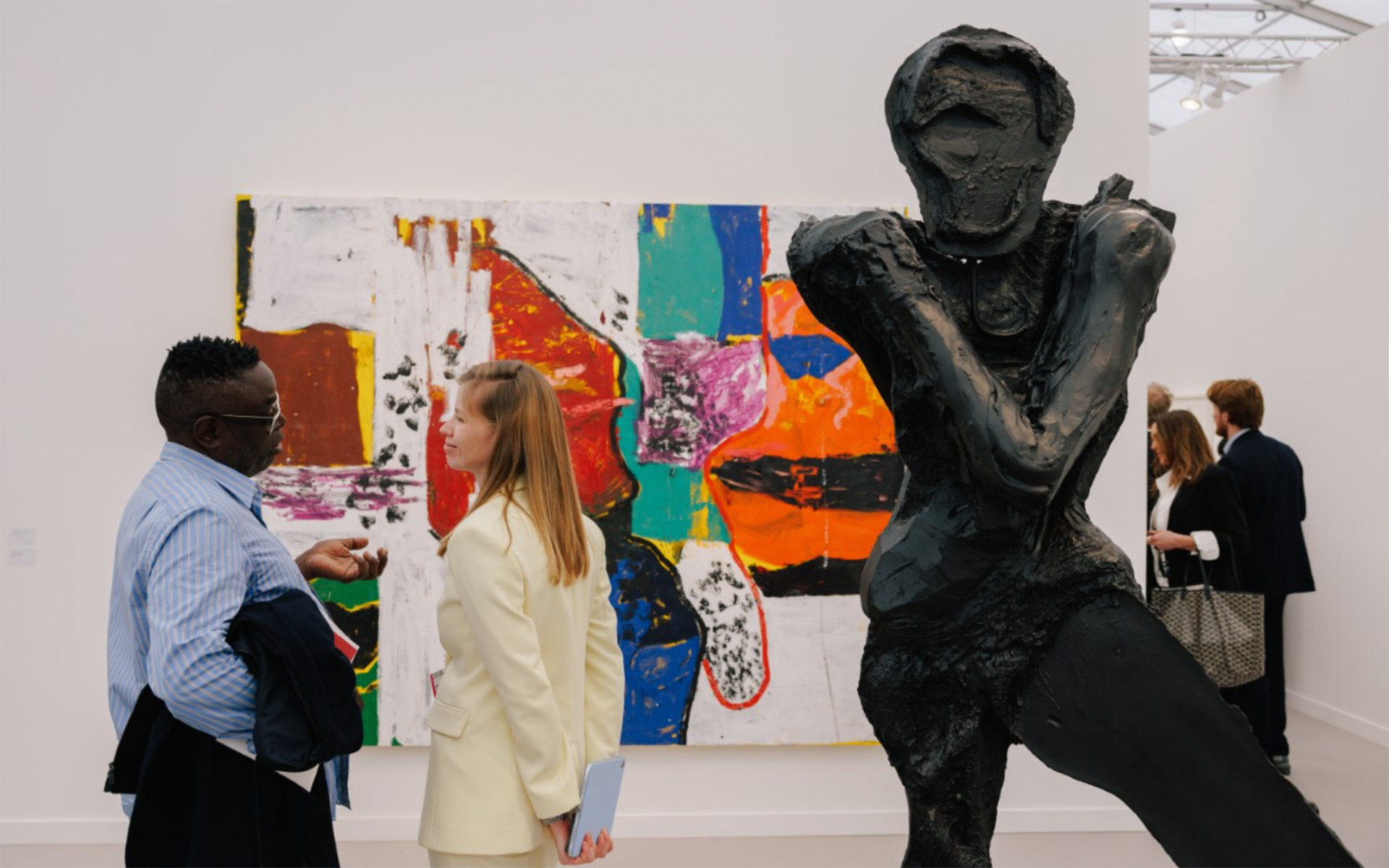 People viewing modern art in a gallery; a large dark sculpture stands prominently in the foreground.