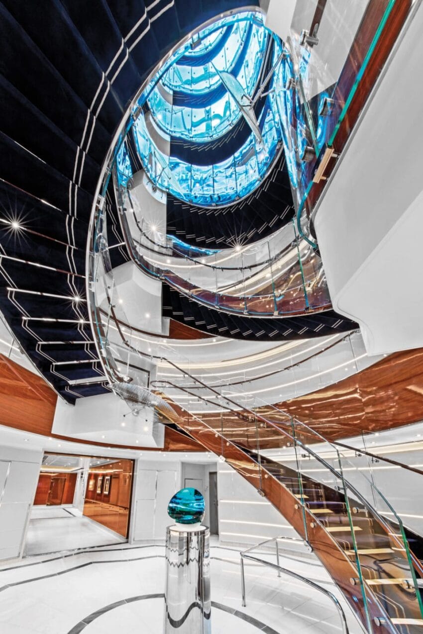 Spiral staircase with glass railings and blue lighting on a luxury yacht, showcasing modern and sleek architectural design.
