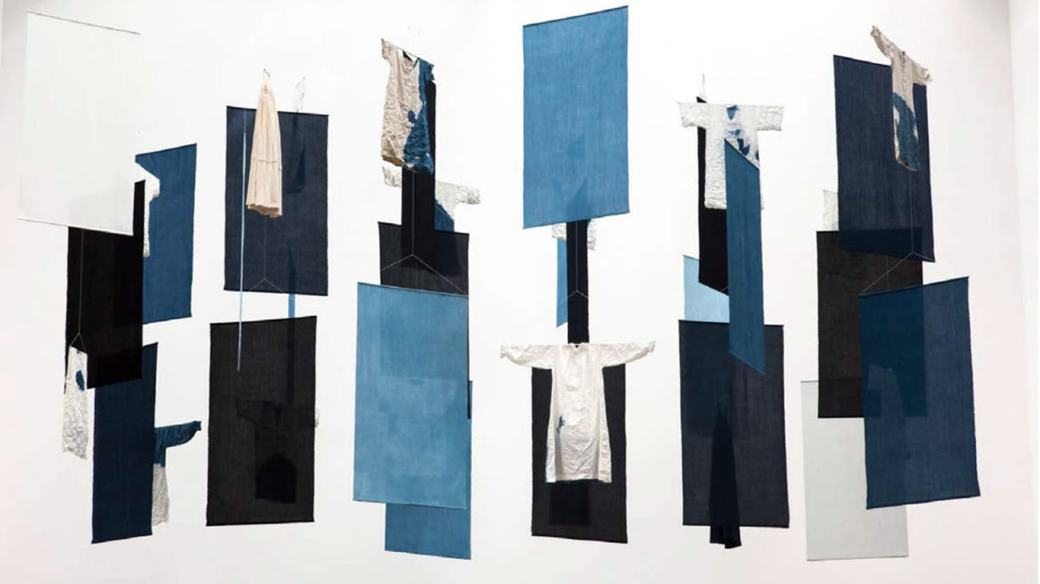 Abstract installation with hanging fabric panels in various shades of blue, black, and white, resembling clothing and geometric shapes.