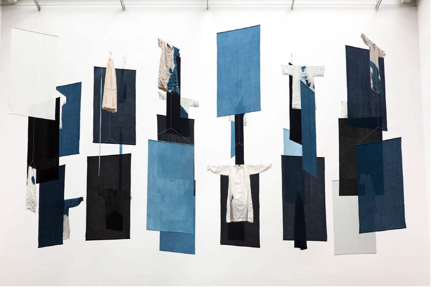 Abstract installation with hanging fabric panels in various shades of blue, black, and white, resembling clothing and geometric shapes.
