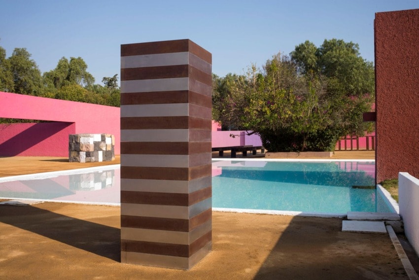 Geometric modern art sculpture near a colorful pool with pink and white walls on a sunny day.