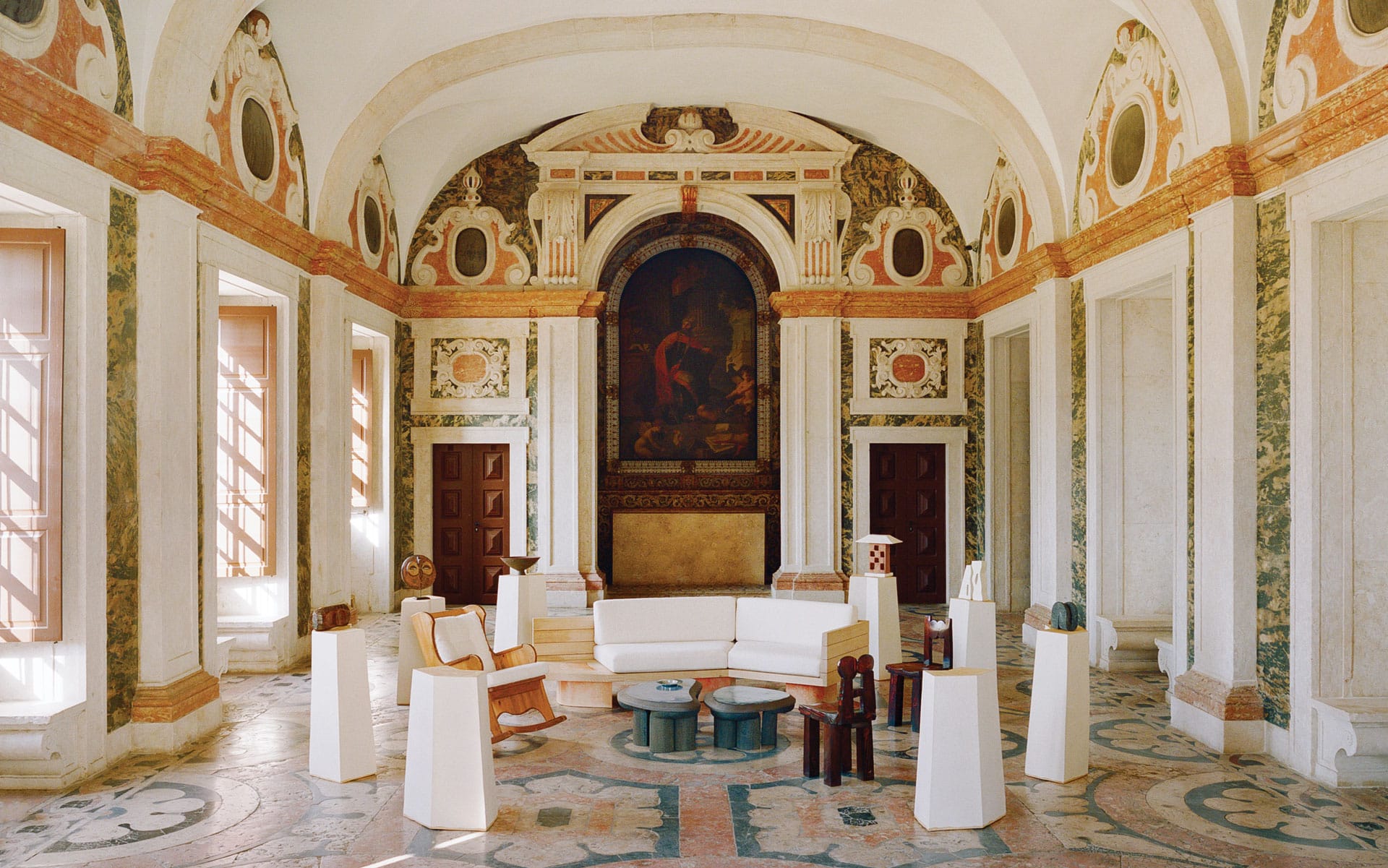Ornate room with classical architecture, colorful frescoes, and modern furniture in natural light.