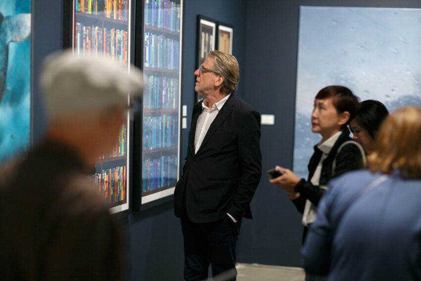 People viewing art exhibits in a gallery, focusing on paintings on a dark blue wall.