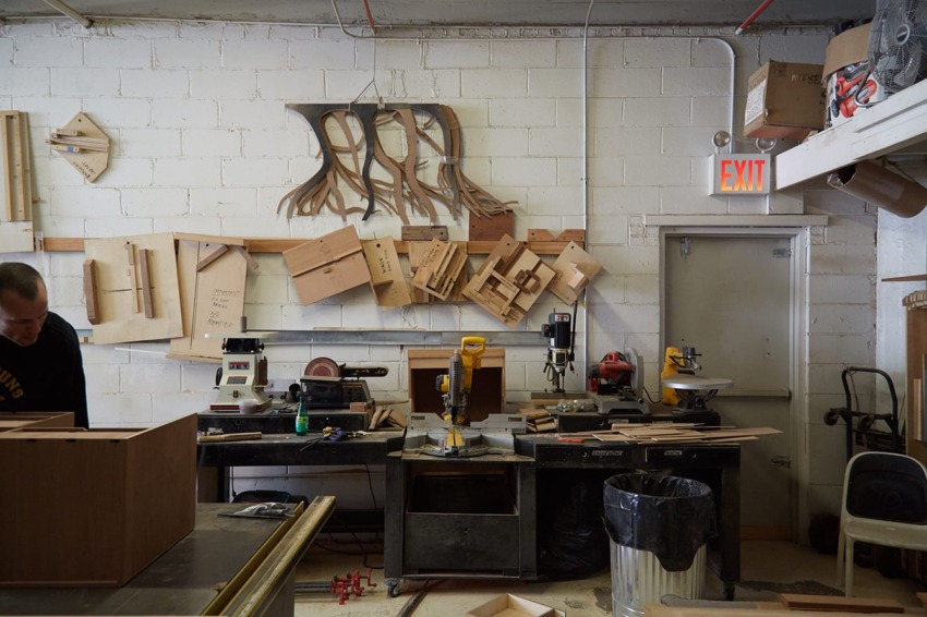 Woodworking workshop with tools, wooden sculptures, and materials organized on shelves and walls.