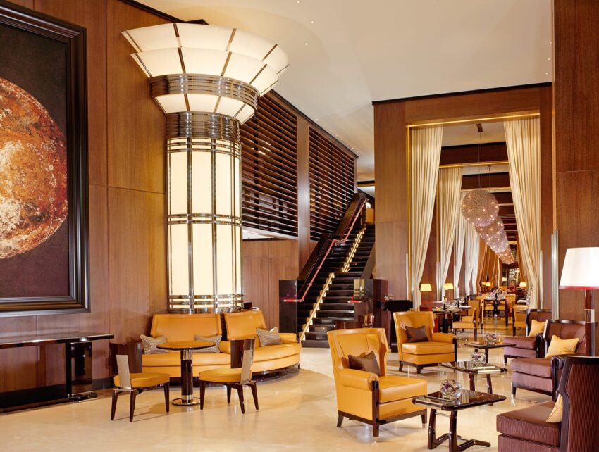 Luxurious hotel lobby with elegant seating, large cylindrical lighting feature, wooden accents, and warm ambient lighting.