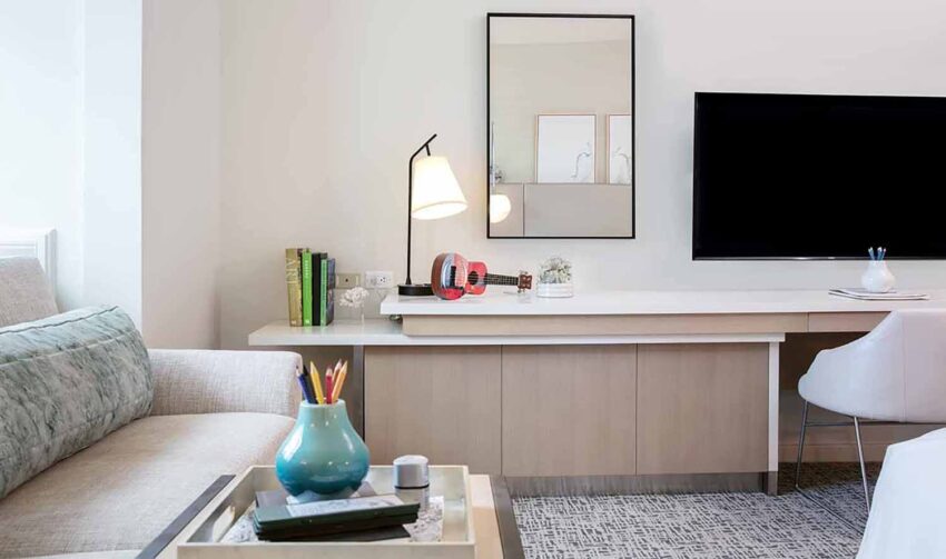 Modern living room with a sleek desk, lamp, and wall-mounted TV, featuring colorful decor and books.