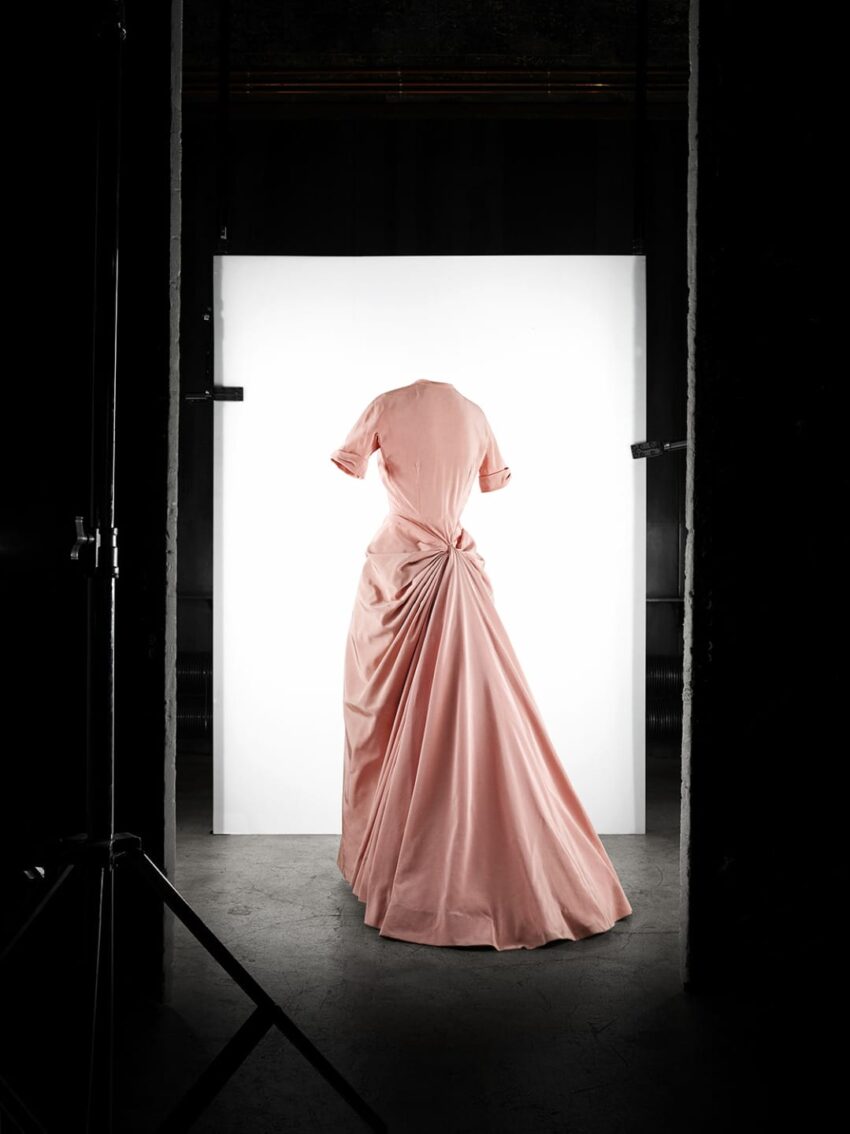 Elegant pink vintage gown on display in a dimly lit studio with a white backdrop.