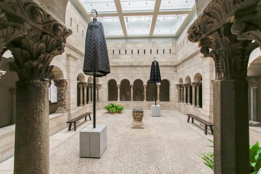 Stone courtyard with ancient columns, sculptures, and two modern black umbrellas suspended from the ceiling.