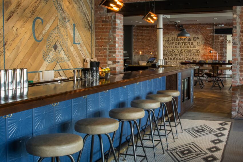 Industrial-style bar interior with blue counter, stools, brick walls, and vintage signage in a cozy atmosphere.