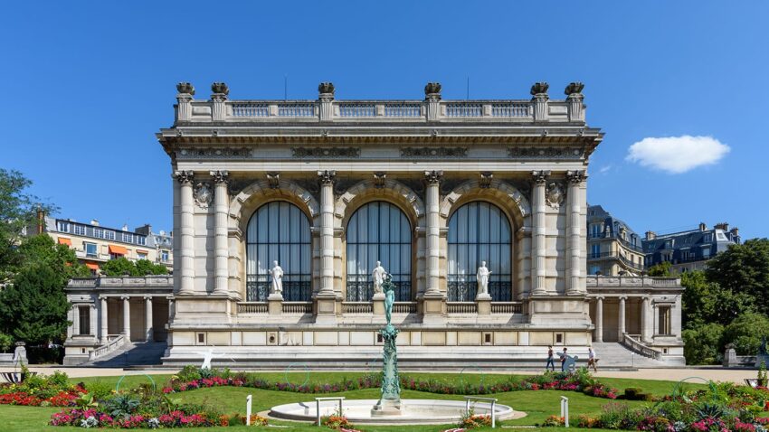 Front view of the Palais Galliera with statues, arched windows, blue sky, and landscaped gardens in Paris.