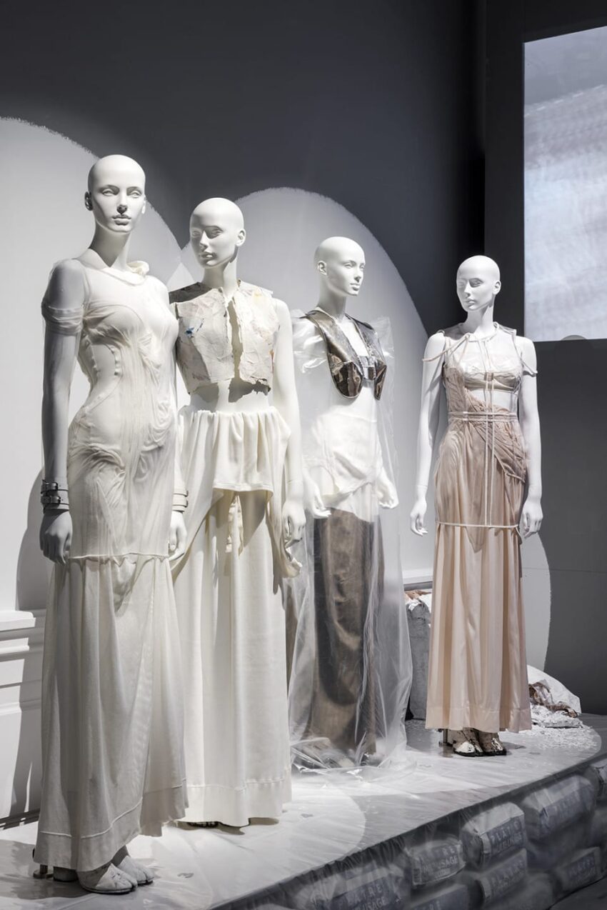 Mannequins dressed in elegant, light-colored gowns displayed in a modern fashion exhibition setting.