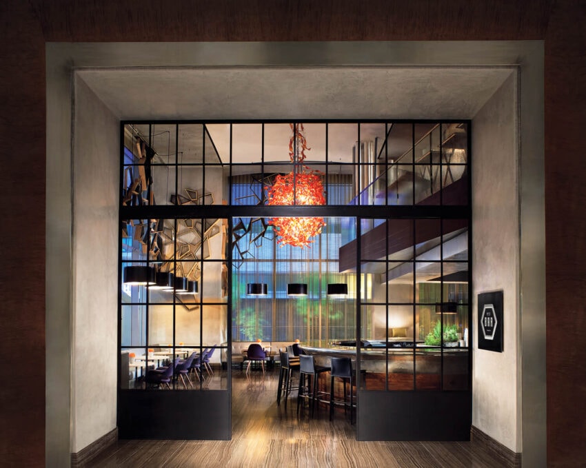 Modern restaurant interior with glass partitions, contemporary decor, and a vibrant red chandelier at the center.