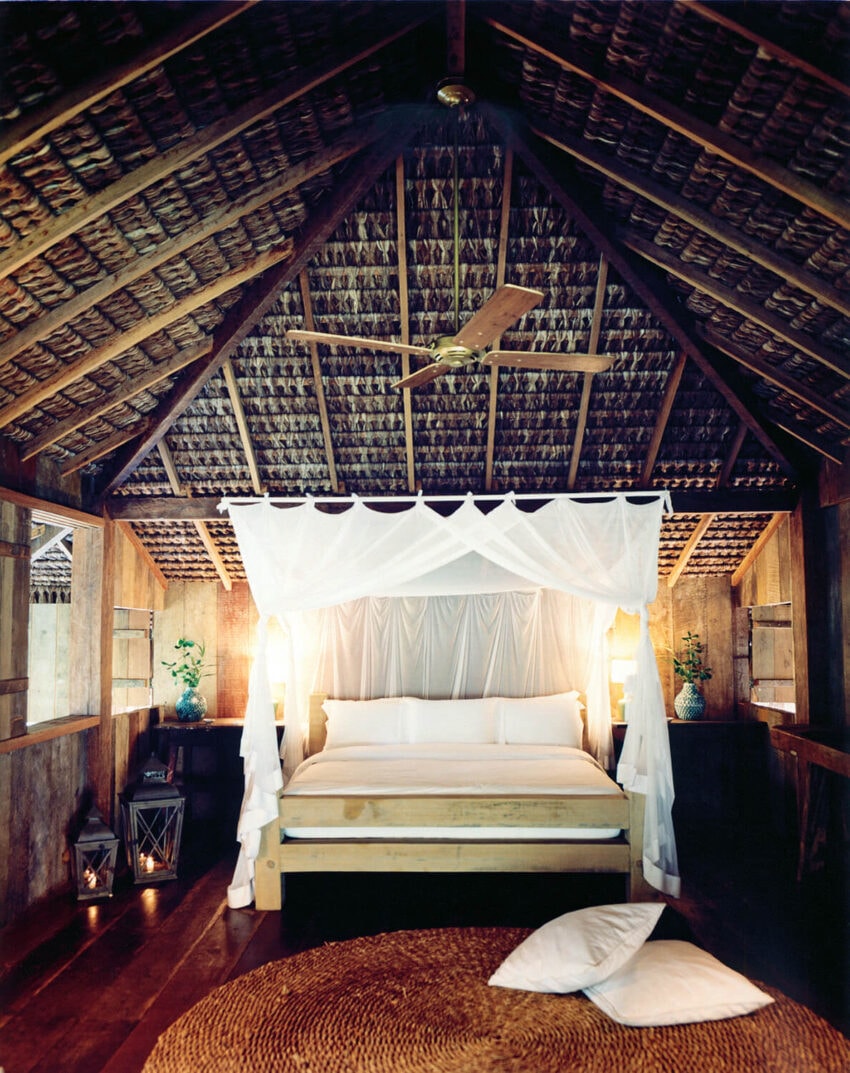 Cozy tropical room with a canopy bed, wooden walls, thatched ceiling, and soft lighting.