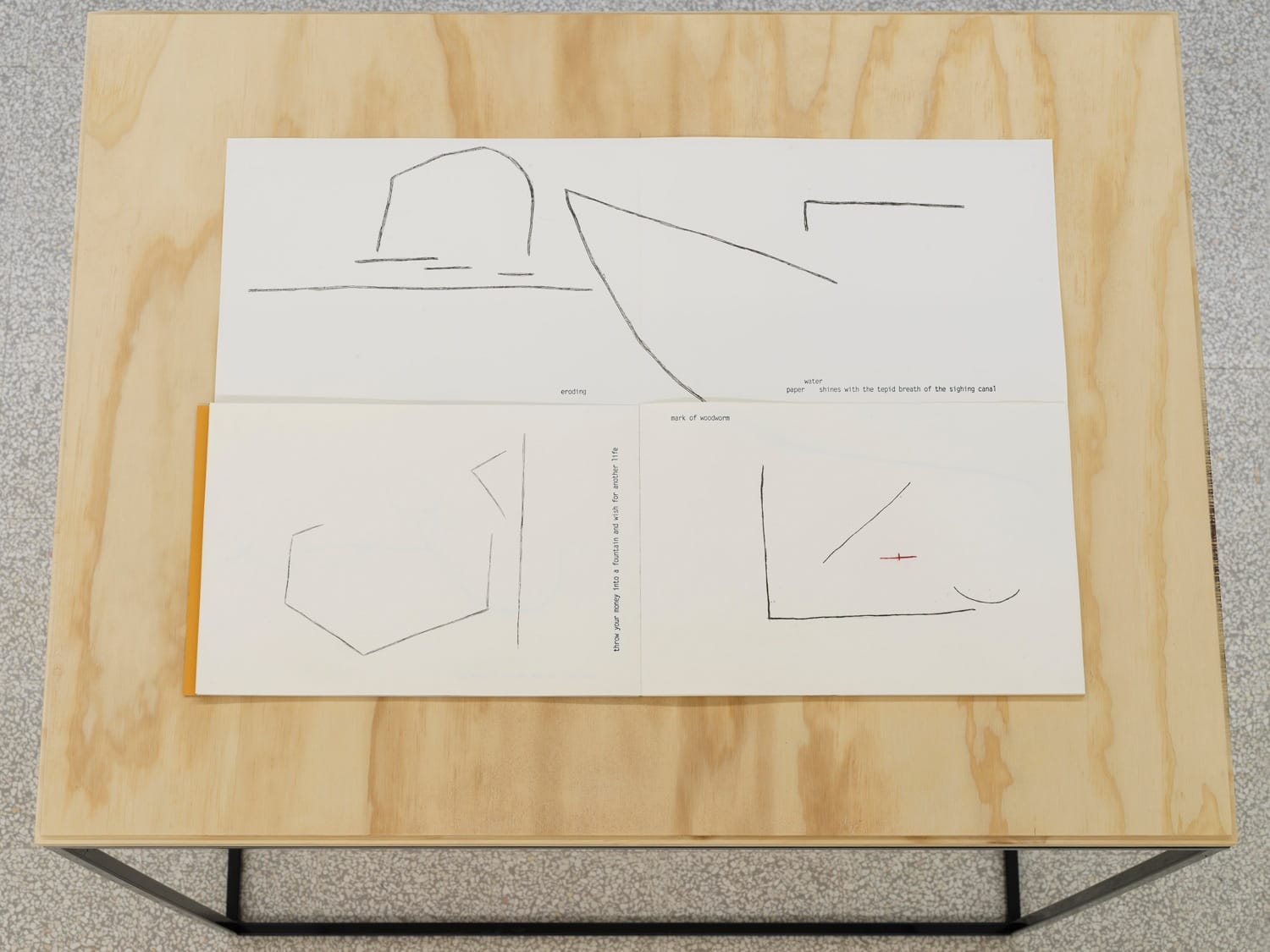 Three abstract line drawings on white paper laid out on a wooden table surface.