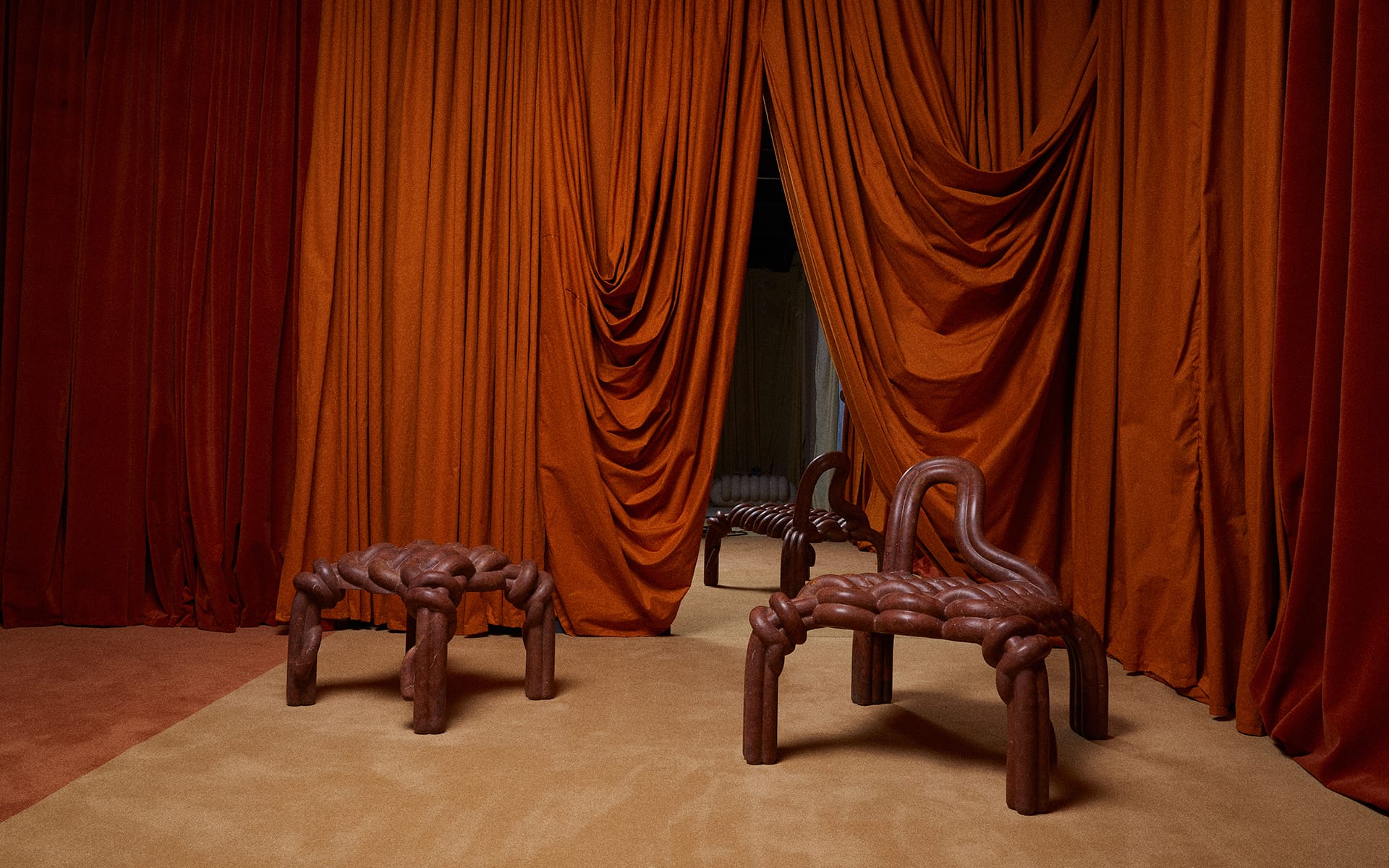A room with orange curtains, two sculptural brown chairs and a mirror reflecting the scene.