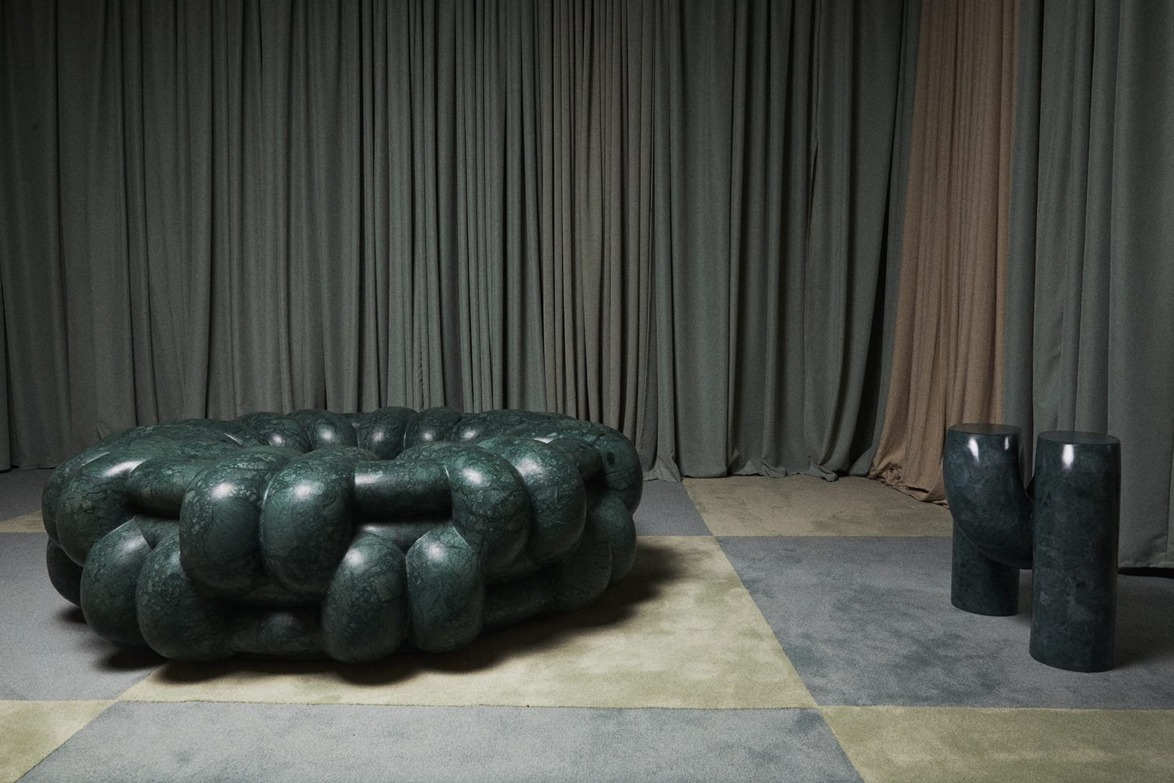 Green marble cushioned furniture and two matching stools against gray curtains and a patterned carpet.