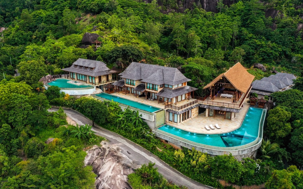 A luxurious villa with a sprawling infinity pool surrounded by lush greenery in a tropical setting.