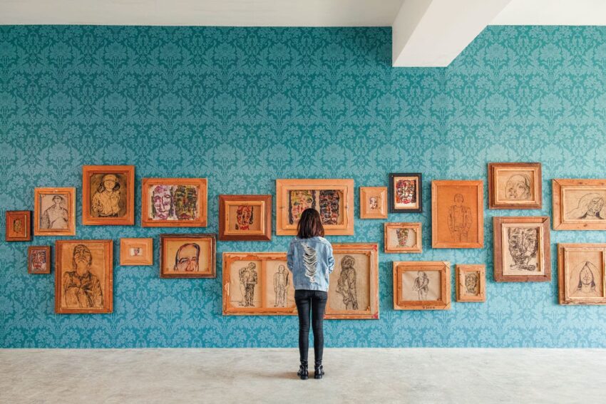 Person viewing a gallery wall with multiple framed artworks on a patterned blue background