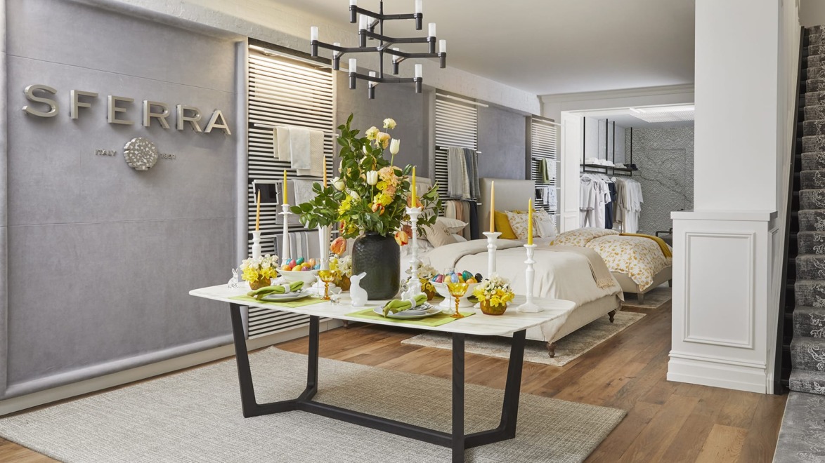 Modern dining area with table set for four, vibrant floral centerpiece, and view into stylishly furnished bedroom in background.