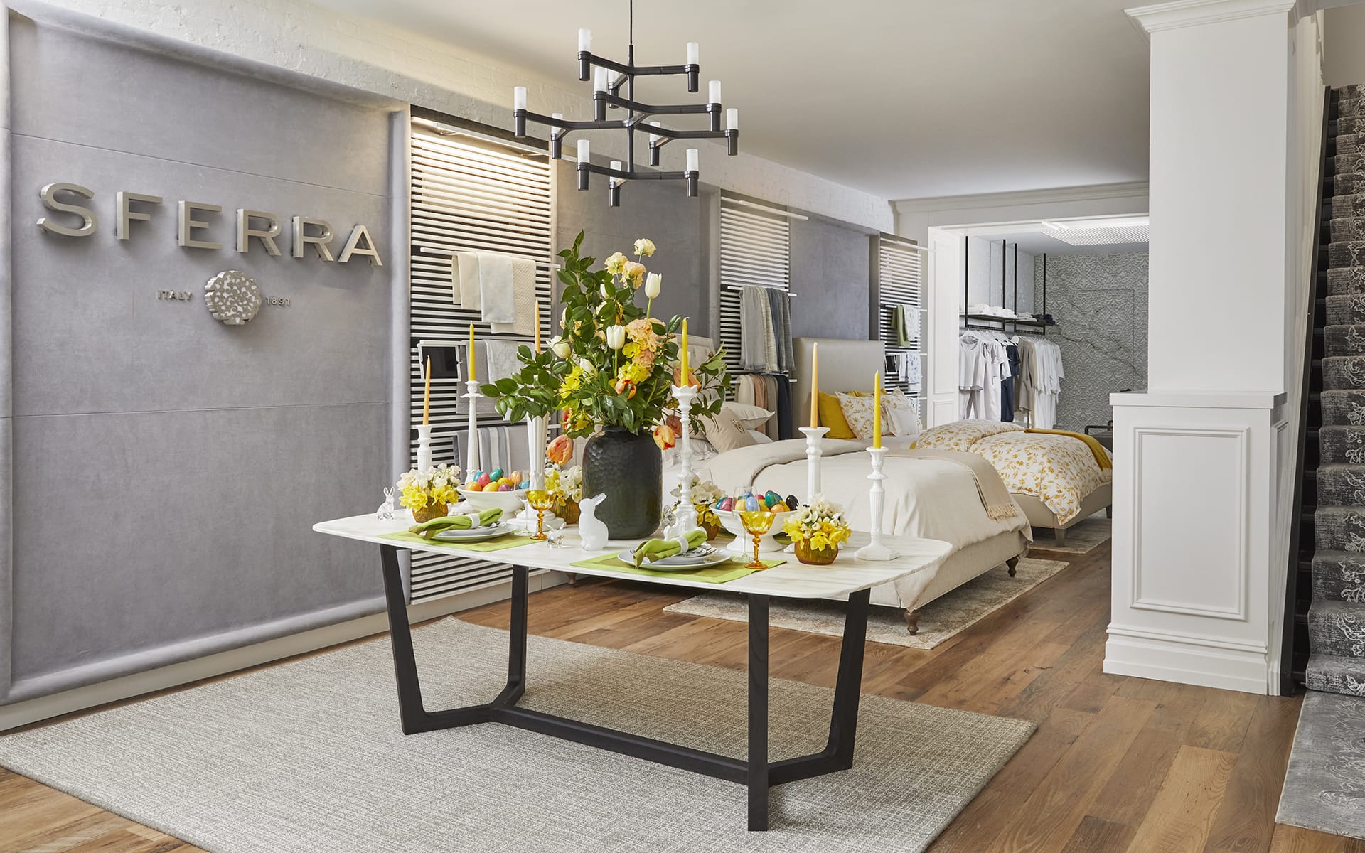 Modern dining area with table set for four, vibrant floral centerpiece, and view into stylishly furnished bedroom in background.