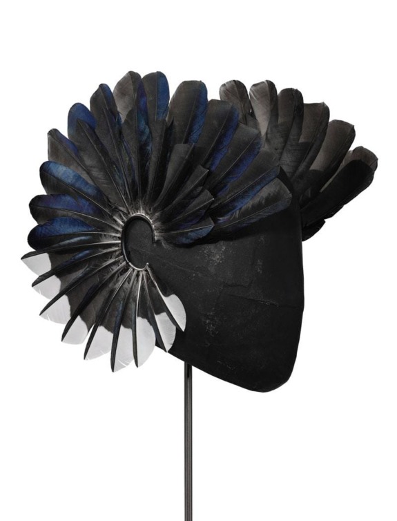 Black and blue abstract feathered headpiece on display stand against white background