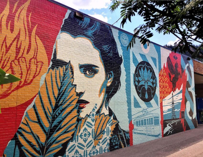 Colorful mural featuring a woman's face and various symbolic elements, including fire, leaves, and geometric shapes.