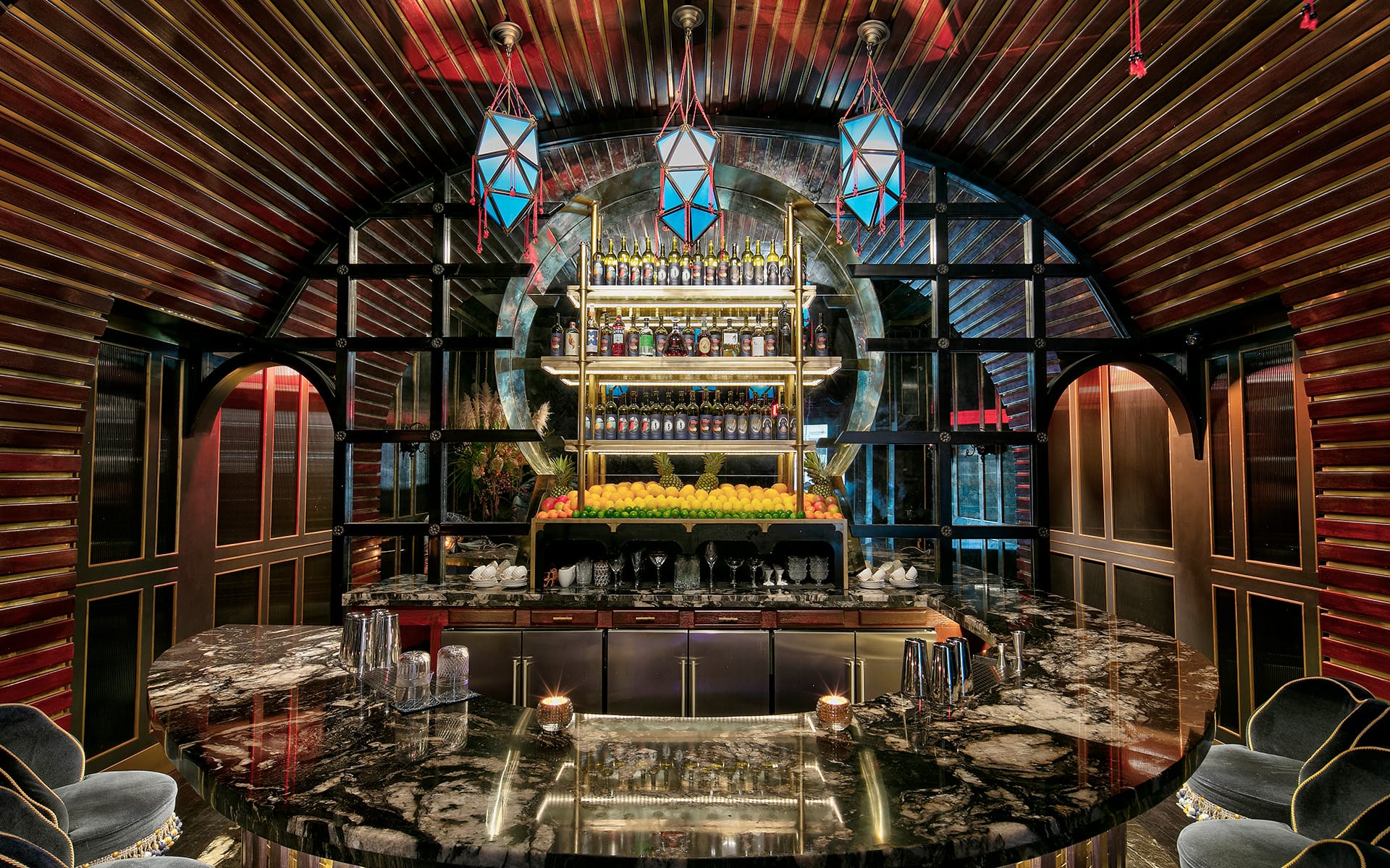 Luxurious bar interior with arched ceiling, elegant lighting, marble countertop, and shelves stocked with colorful bottles and fruit.