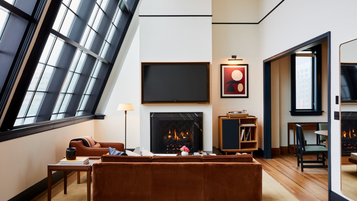 Modern living room with large windows, brown couch, fireplace, and contemporary decor in an airy, angled ceiling space.