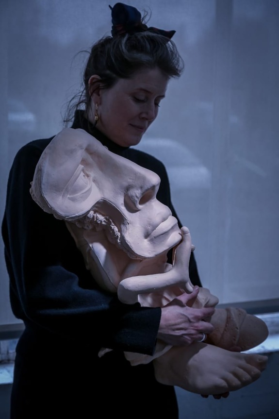 Person holding a large sculpted head with a thoughtful expression in a dimly lit room.