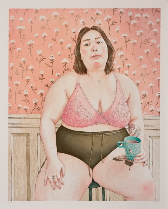 Woman in pink lace top sitting with a mug, floral wallpaper background.