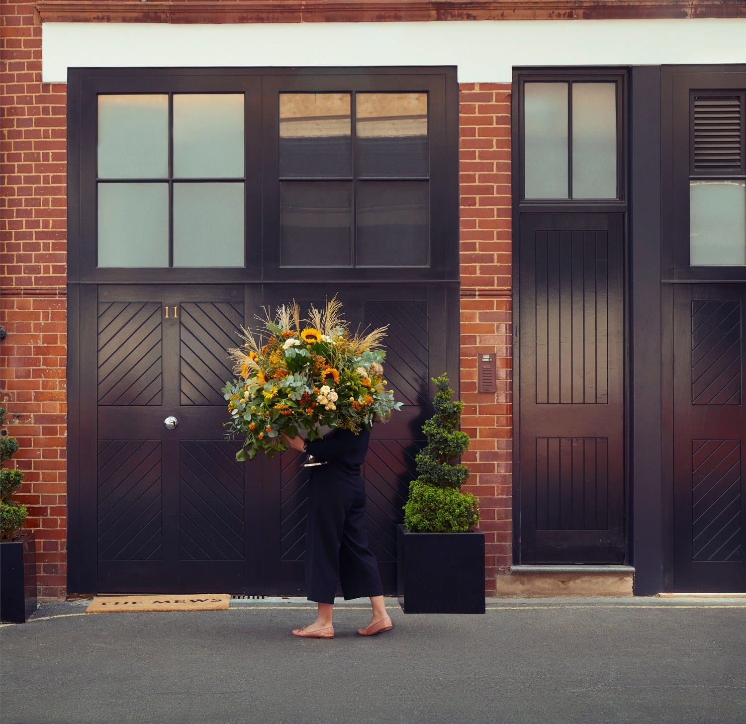 Person carrying a large bouquet of flowers in front of a brick building with black doors and windows.