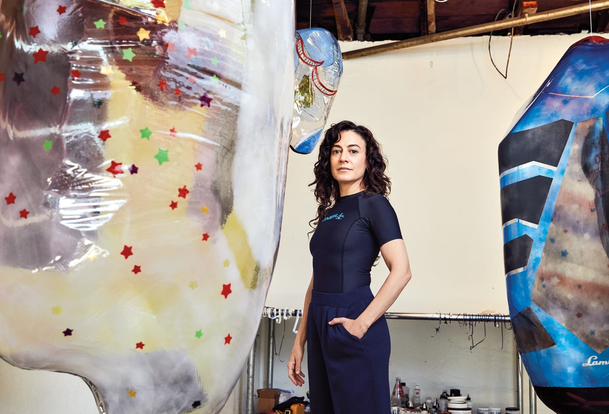 Woman standing in an art studio surrounded by large colorful sculptures with star patterns and abstract designs.