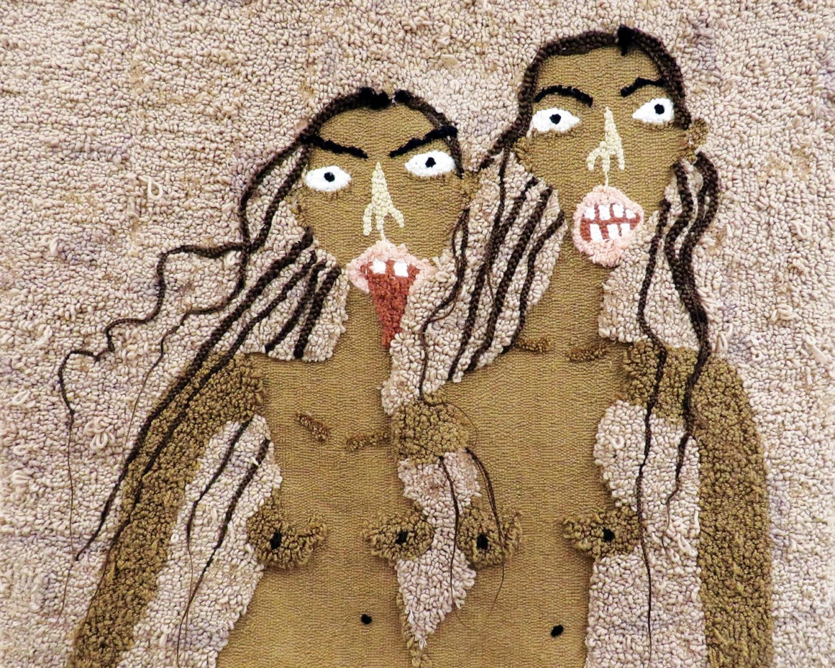 Textile art depicting two abstract human figures with long hair and expressive faces, created with textured fabric.