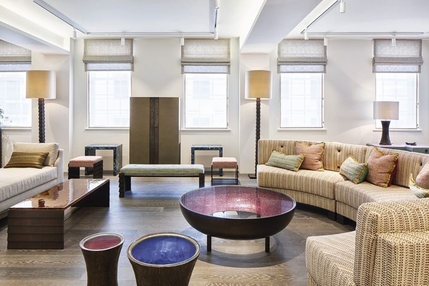 Modern living room with beige sofas, wooden coffee table, round colorful centerpiece, and floor lamps by large windows.