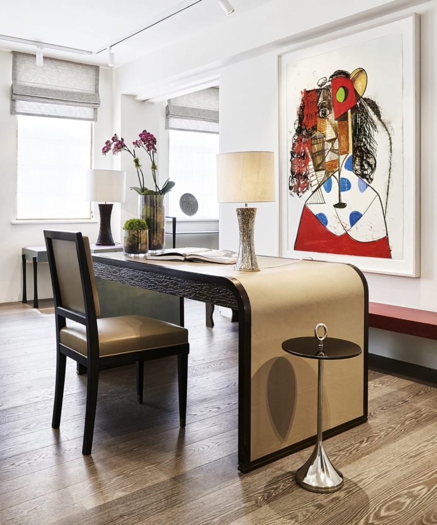 Modern office with abstract art, decorative lamps, orchids on a desk, and a small round side table on wooden flooring.