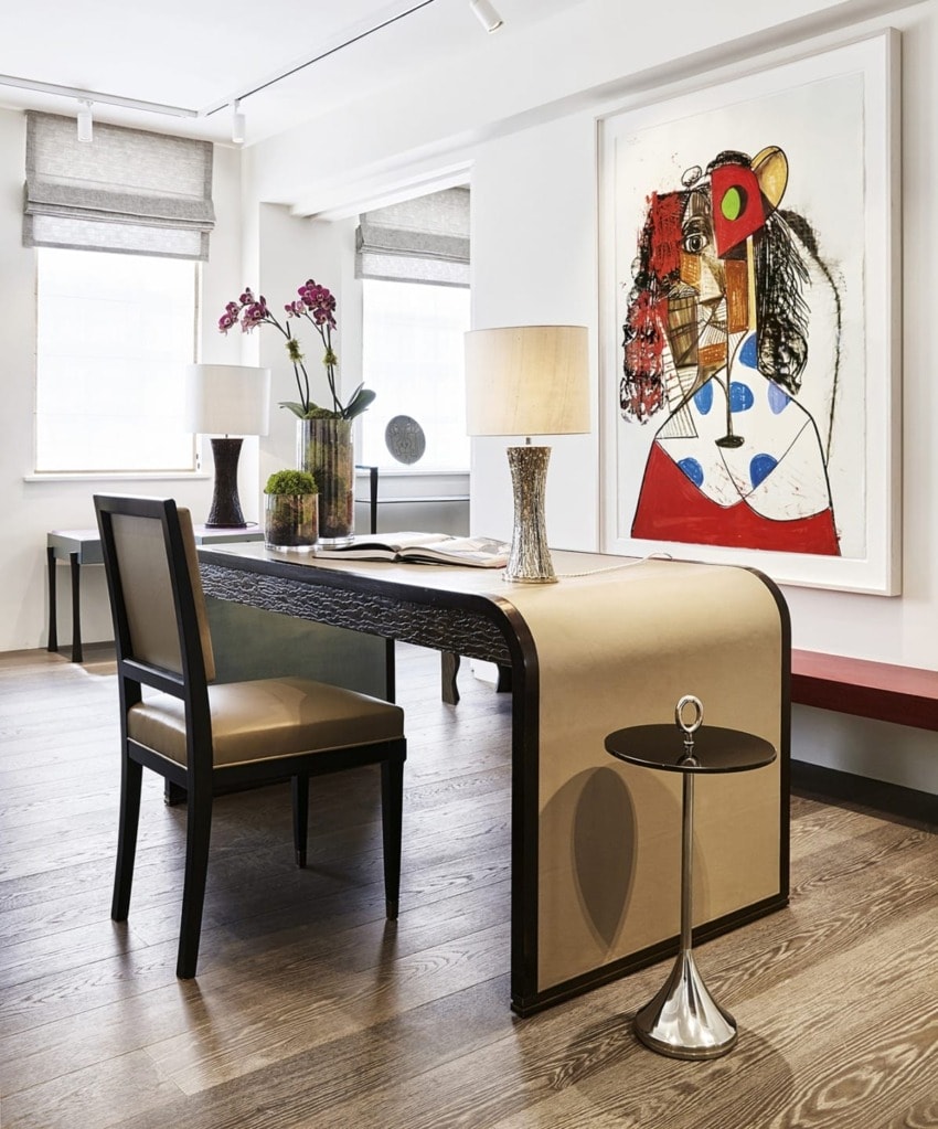 Modern office with abstract art, decorative lamps, orchids on a desk, and a small round side table on wooden flooring.