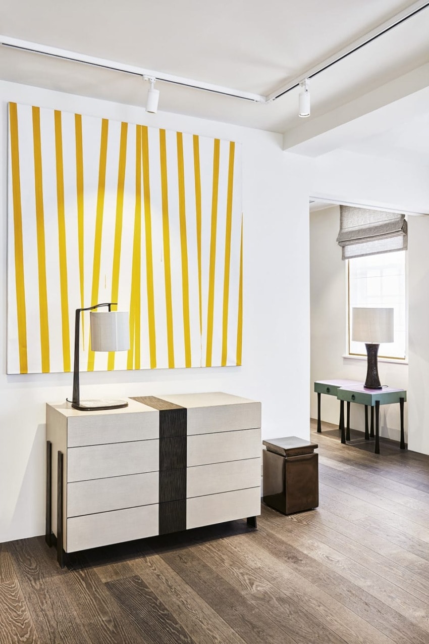 Modern living room with striped yellow wall art, beige dresser, and table lamps on a wooden floor.