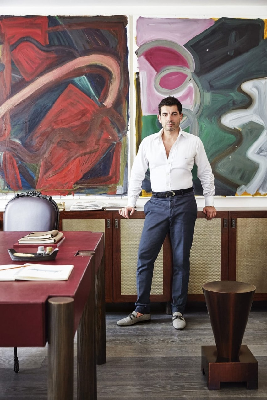 Man standing against a cabinet in an art gallery with abstract paintings in the background.