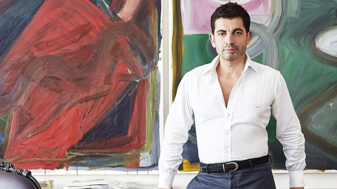 Man in white shirt stands in front of colorful abstract paintings in an art studio.