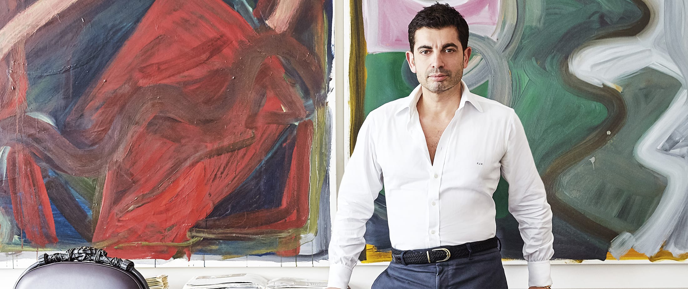 Man in white shirt stands in front of colorful abstract paintings in an art studio.